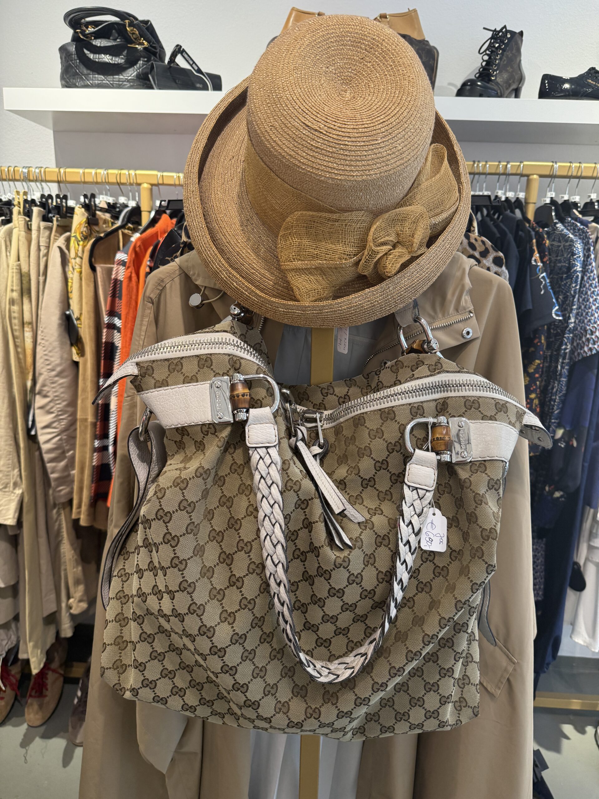 Gucci-Tasche und Strohhut über einem Trenchcoat im Laden von ARTEMODA